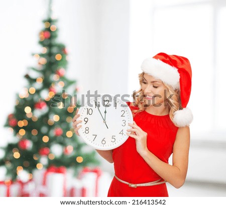 winter holidays, time and people concept - smiling woman in santa helper hat with clock over living room and christmas tree background