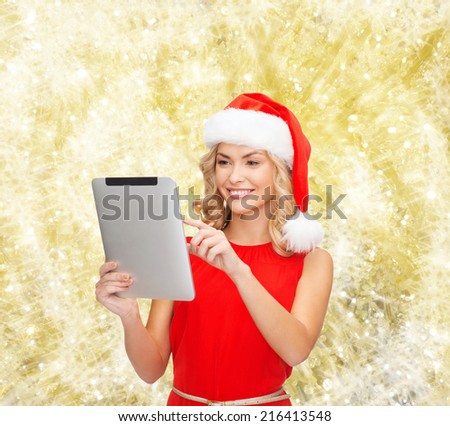 christmas, technology, present and people concept - smiling woman in santa helper hat with tablet pc computer over yellow lights background