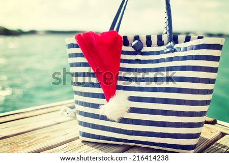 beach, summer, vacation, christmas and accessories concept - close up of beach bag and santa helper hat on wooden pier