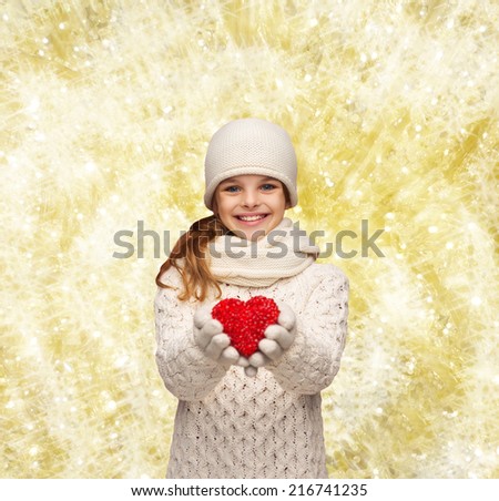 christmas, holidays, childhood, presents and people concept - dreaming girl in winter clothes with red heart over yellow lights background