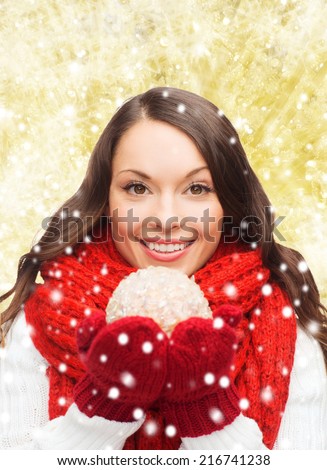 happiness, winter holidays and people concept - smiling young woman in red scarf and mittens with christmas ball over yellow lights background