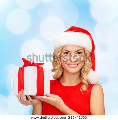 christmas, holidays, celebration and people concept - smiling woman in santa helper hat with gift box over blue lights background