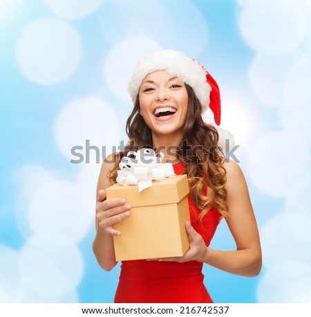 christmas, holidays, celebration and people concept - smiling woman in santa helper hat with gift box over blue lights background
