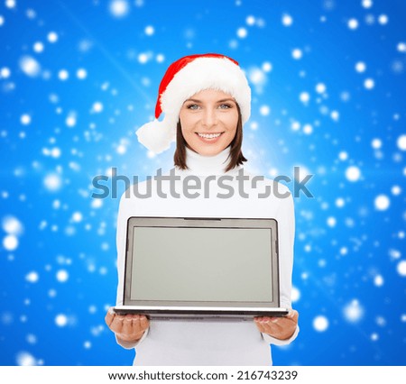 christmas, technology, winter holidays and people concept - smiling woman in santa helper hat with blank screen laptop computer over blue snowy background