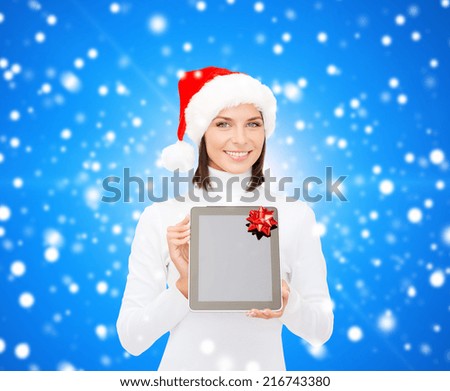 christmas, technology, present and people concept - smiling woman in santa helper hat with blank screen tablet pc computer over blue snowy background