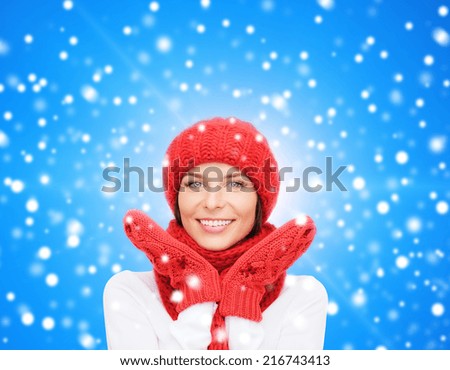 happiness, winter holidays, christmas and people concept - smiling young woman in red hat, scarf and mittens over blue snowy background
