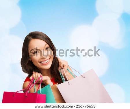 happiness, winter holidays, christmas and people concept - smiling young woman with shopping bags over blue lights background