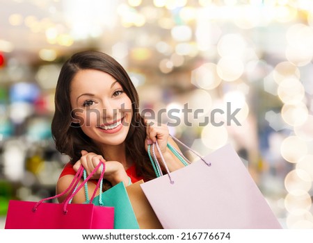 happiness, winter holidays, christmas and people concept - smiling young woman with shopping bags over lights background