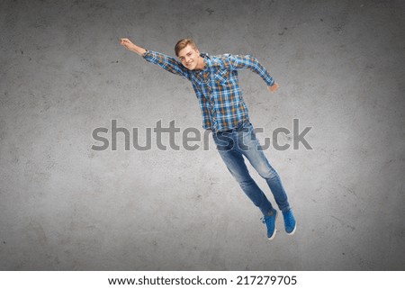 happiness, freedom, movement and people concept - smiling young man jumping in air over concrete wall background