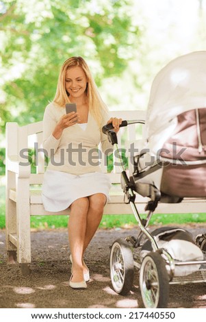 family, parenthood, technology and people concept - happy mother with with smartphone and baby stroller in park