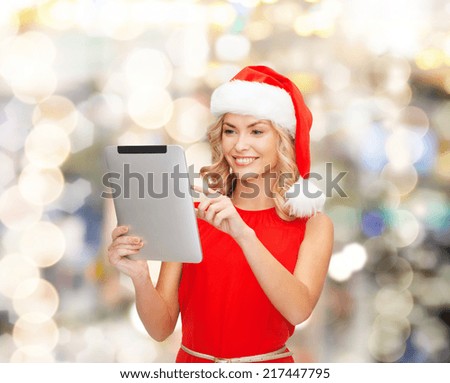 christmas, technology, present and people concept - smiling woman in santa helper hat with tablet pc computer over lights background