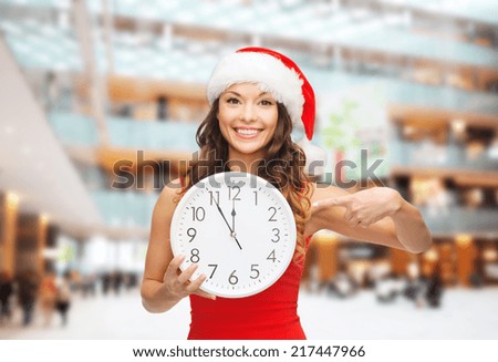 christmas, winter, holidays, time and people concept - smiling woman in santa helper hat and red dress with clock over shopping center background