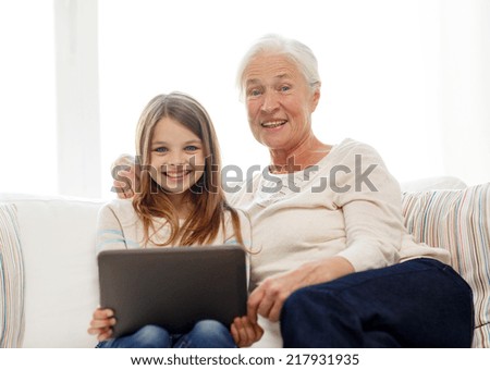 family, generation, technology and people concept - smiling granddaughter and grandmother with tablet pc computer sitting on couch at home