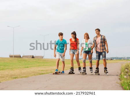 holidays, vacation, love and friendship concept - group of smiling teenagers with roller skates and skateboard riding outdoors