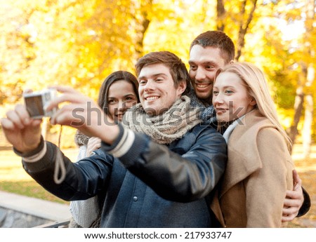 relationship, season, friendship, technology and people concept - group of smiling men and women making self portrait with digital camera in autumn park