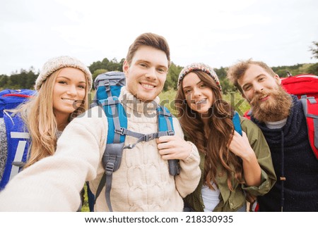 adventure, travel, tourism, hike and people concept - group of smiling friends with backpacks making selfie outdoors