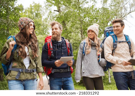 adventure, travel, tourism, hike and people concept - group of smiling friends with backpacks and tablet pc computer walking outdoors