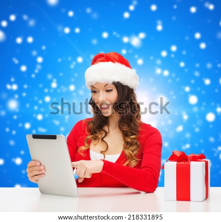 christmas, holidays, technology and people concept - smiling woman in santa helper hat with gift box and tablet pc computer over blue snowing background