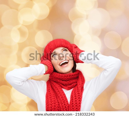happiness, winter holidays, christmas and people concept - smiling young woman in red hat, scarf and mittens over beige lights background