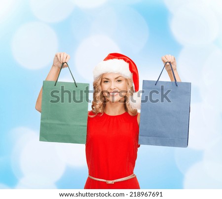 sale, gifts, christmas, holidays and people concept - smiling woman in red dress and santa helper hat with shopping bags over blue lights background