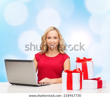 christmas, holidays, technology, advertising and people concept - smiling woman in red blank shirt with gifts and laptop computer over blue lights background