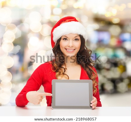 christmas, holidays, technology and people concept - smiling woman in santa helper hat with tablet pc computer over lights background