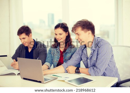 education, technology, school and internet concept - three smiling students with laptop, tablet pc and notebooks at school