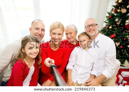 family, holidays, generation, christmas and people concept - smiling family with camera and selfie stick making picture at home