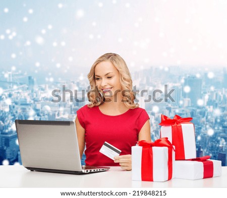 christmas, holidays, technology and shopping concept - smiling woman in red blank shirt with gift boxes, credit card and laptop computer over blue lights background