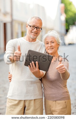 age, tourism, travel, technology and people concept - senior couple with tablet pc computer showing thumbs up gesture on street