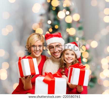 christmas, holidays,  family and people concept - happy mother, father and little girl in santa helper hats with gift boxes over living room and christmas tree background
