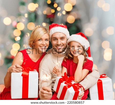 christmas, holidays,  family and people concept - happy mother, father and little girl in santa helper hats with gift boxes over living room and christmas tree background