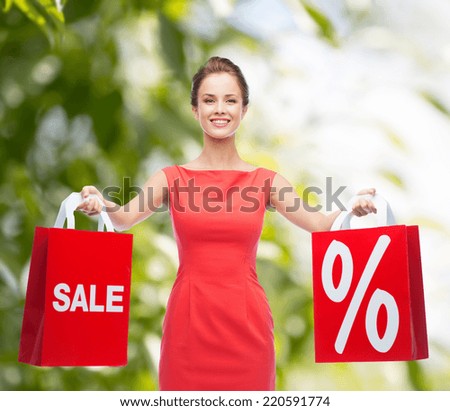 shopping, sale, gifts, christmas and holiday concept - smiling young woman in red dress with shopping bags with percent and sale sign
