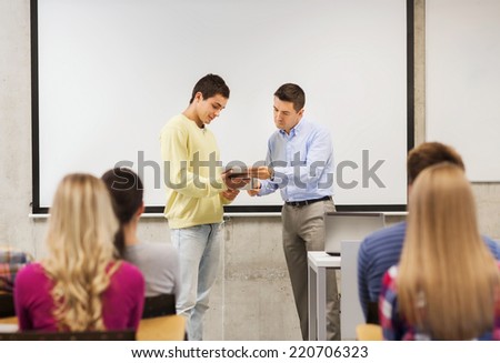 education, high school, technology and people concept - smiling student boy with tablet pc, laptop computer standing in front of students and teacher in classroom