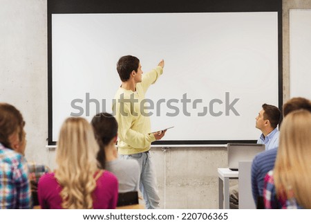 education, high school, technology and people concept - smiling student boy with tablet pc, laptop computer standing in front of students and teacher in classroom