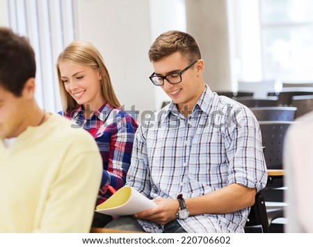 education, high school, teamwork and people concept - group of smiling students with notebook sitting in lecture hall and writing
