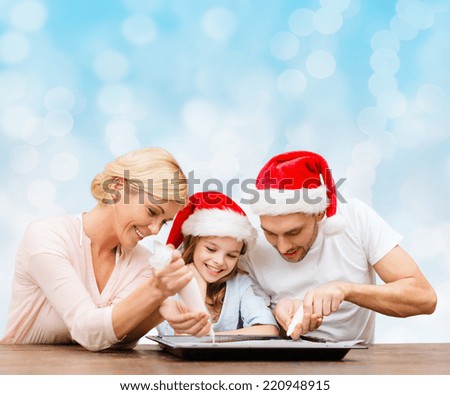 food, family, christmas, happiness and people concept - smiling family in santa helper hats with glaze and pan cooking over blue lights background