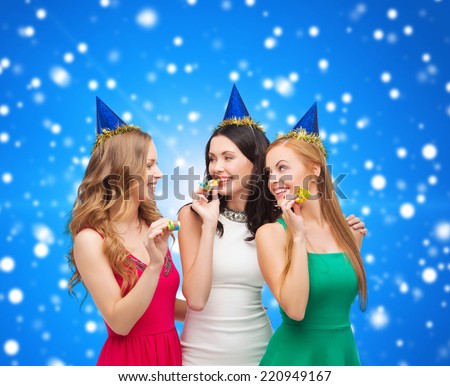holidays, people and celebration concept - smiling women in party caps blowing to whistles over blue snowing background