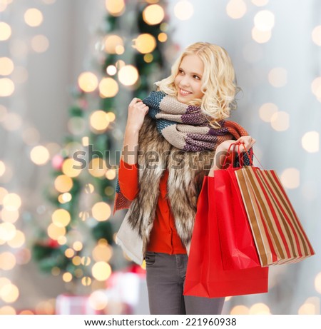 happiness, winter holidays and people concept - smiling young woman in winter clothes with red shopping bags over christmas tree background