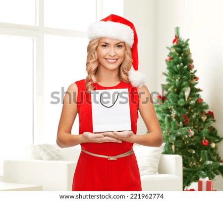 advertisement, holydays and sale concept - smiling woman in santa helper hat with white blank shopping bag over living room with christmas tree background