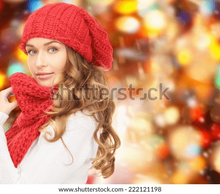 happiness, winter holidays, christmas and people concept - young woman in hat and scarf over red lights background