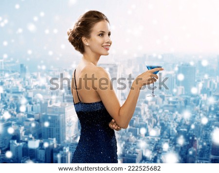 drinks, christmas, holidays and people concept - smiling woman in evening dress holding cocktail over snowy city background