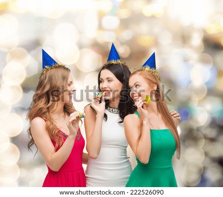 holidays, people and celebration concept - smiling women in party caps blowing to whistles over lights background