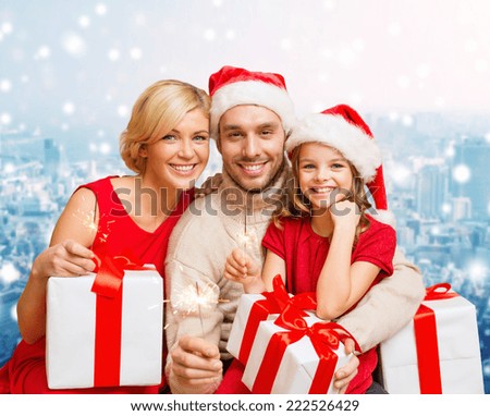 christmas, holidays,  family and people concept - happy mother, father and little girl in santa helper hats with gift boxes over snowy city background