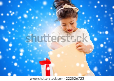 holidays, presents, christmas, childhood and people concept - smiling little girl girl with gift box over blue lights background