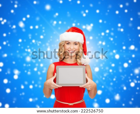 christmas, technology, present and people concept - smiling woman in santa helper hat with tablet pc computer showing blank screen over blue lights background