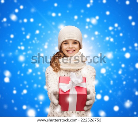 christmas, holidays, childhood, presents and people concept - dreaming girl in winter clothes with gift box over blue snowing background