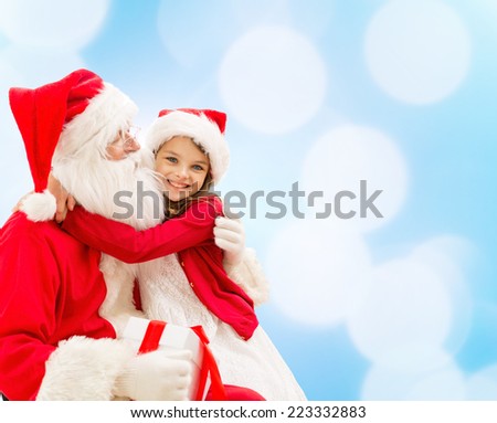 holidays christmas childhood and people concept smiling little girl hugging with santa claus over blue lights background holidays christmas childhood and people concept smiling little girl hugging with santa claus over blue lights background