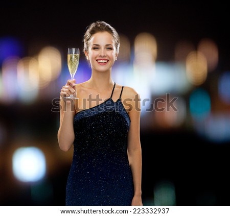 party, drinks, holidays, people and celebration concept - smiling woman in evening dress with glass of sparkling wine over night lights background