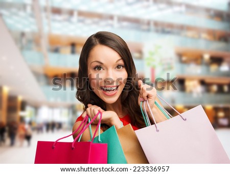sale, gifts, holidays and people concept - smiling woman with colorful bags over shopping center background